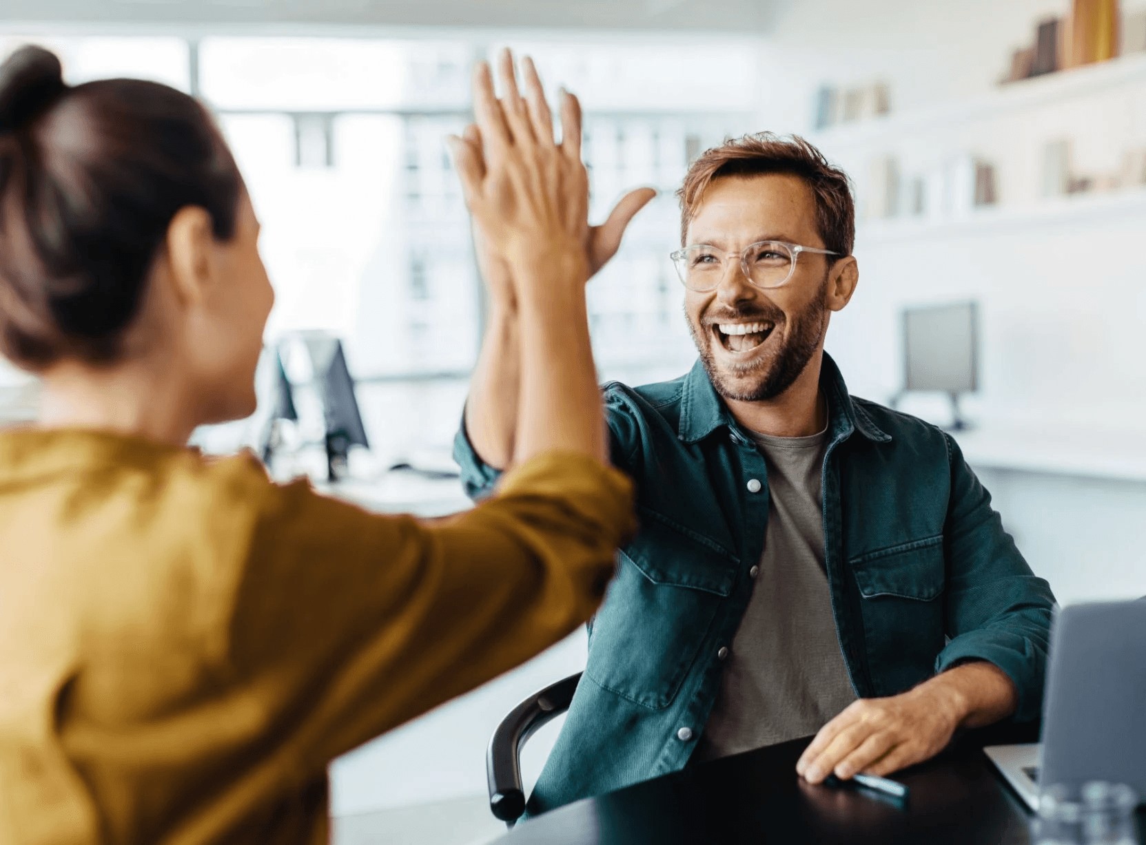 Two colleagues high-fiving and smiling in an office.